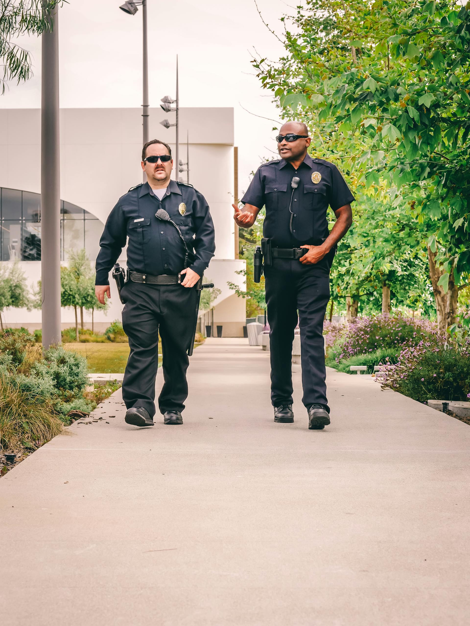 Two police officers walking down a pathway in a city park, engaged in conversation.